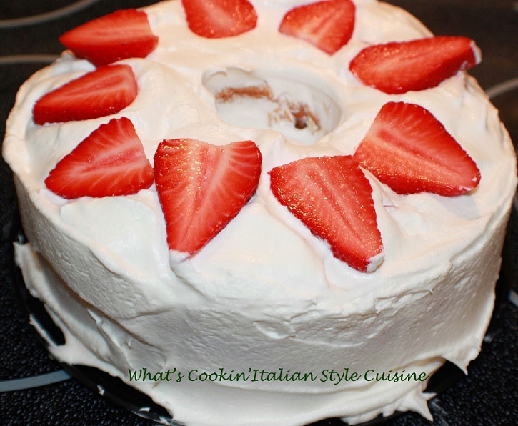 This is an angel food cake with a tunnel inside and filled with strawberry cheesecake filling. This one has heavy cream no sugar and strawberries on top. The cake is on a large plate. This is how to make a tunnel cake filled with cheesecake no sugar pudding, whipped cream and strawberries