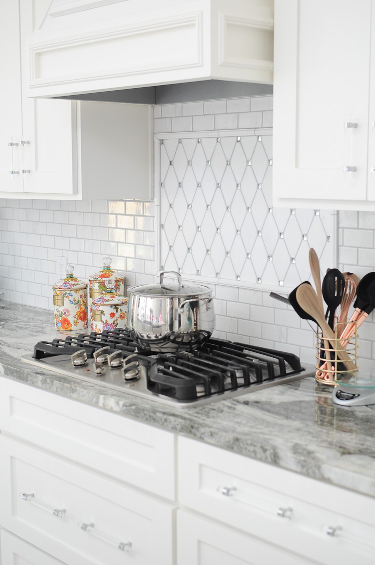 A bright white kitchen with a jeweled backsplash and flower market canisters by MacKenzie-Childs. A bright white kitchen with a jeweled backsplash and flower market canisters by MacKenzie-Childs.