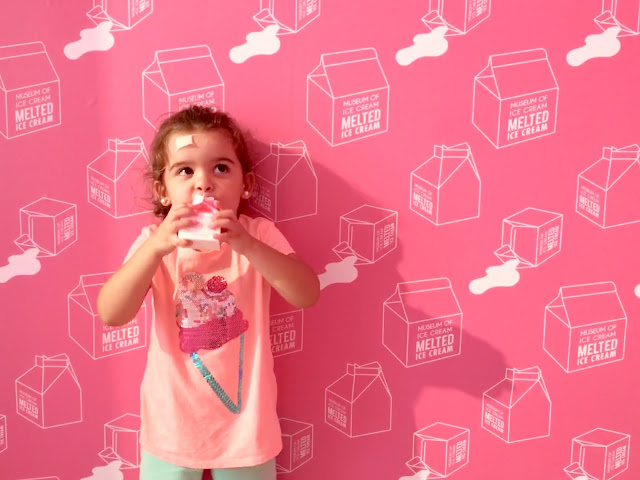 Leia's favorite frozen treat from the museum A toddler girl drinking from a pink milk carton in front of a wall with a pink milk cartons print