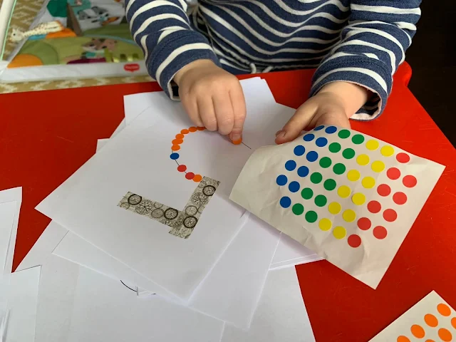 A toddler sticking sticky dots onto the number 5