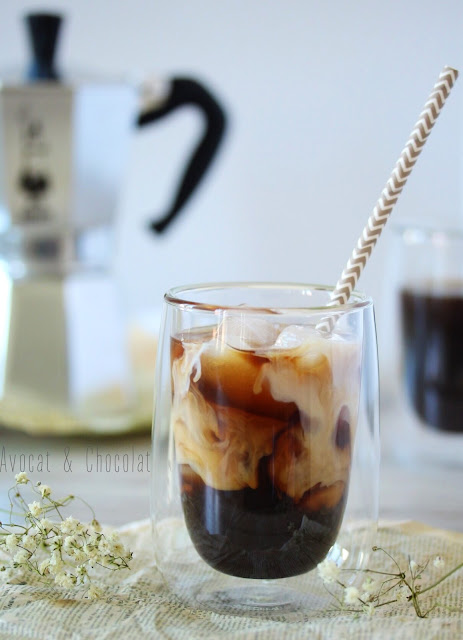 alt="iced coffee dans un joli verre rempli de glaçons, la crème se mélange gentiment au café et en arrière plan une cafetière italienne"