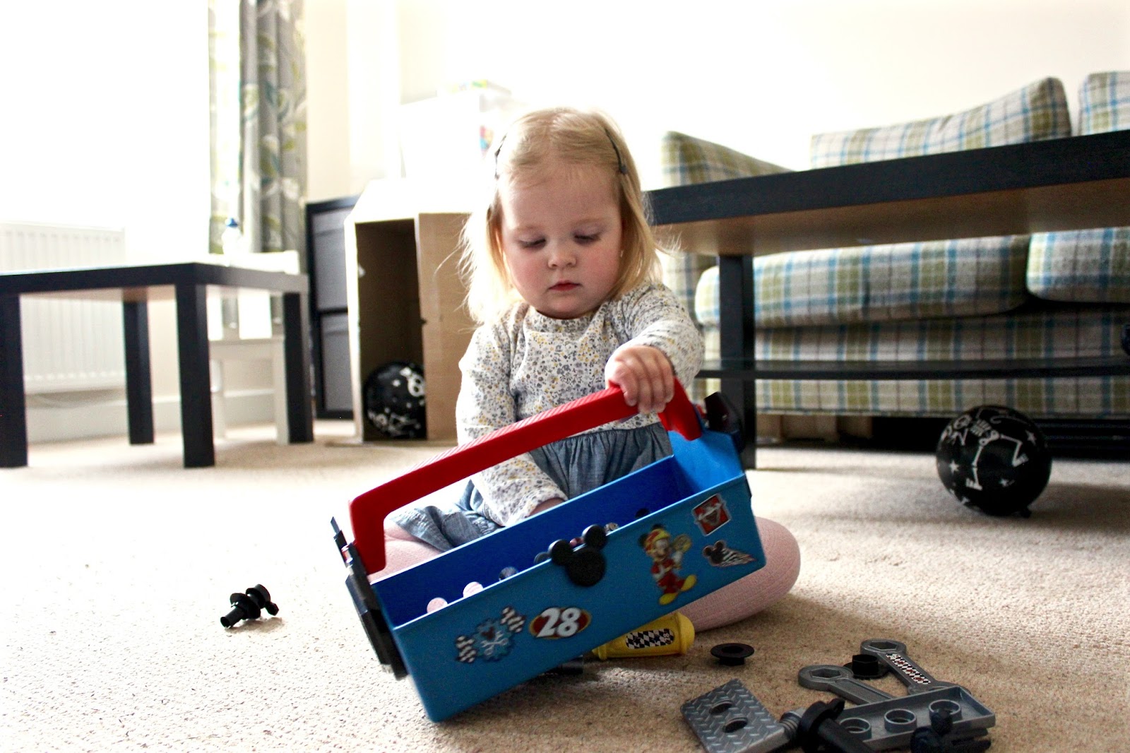 Elise (aged 2) is holding up the pit crew tool box and looking at the side of it whilst putting screws in the existing holes.