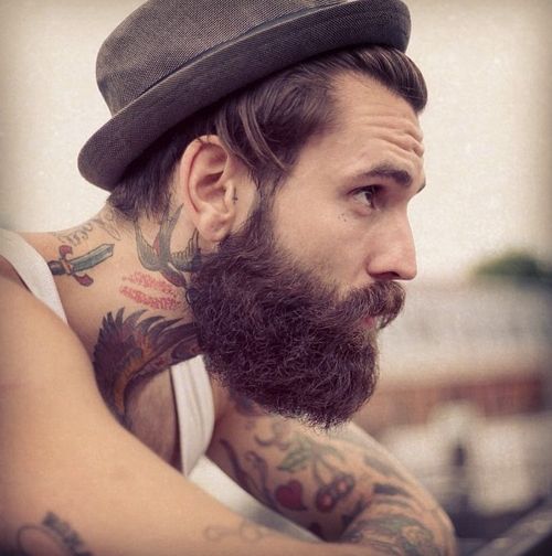 Hombre con barba y sombrero mirando hacia el horizontes, lleva tatuajes tradicionales en los brazos