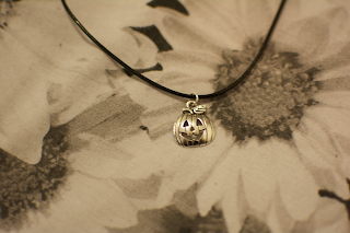 A pumpkin charm on a thin choker, with an empty casket review bag in background