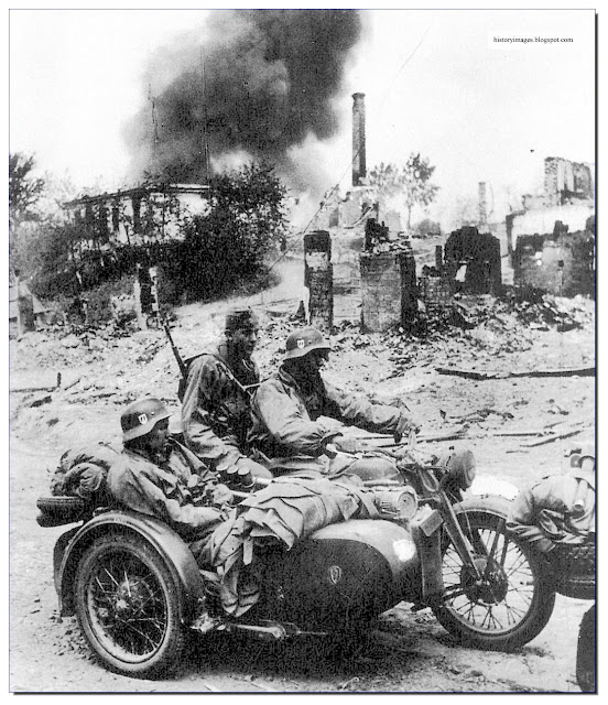 Liebstandarte soldiers ride  motor-cycle through  destroyed Russian village