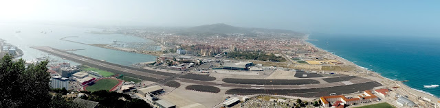 Aerial-style photo of the entire border between La Linea de la Concepcion, Spain, and the British territory of Gibraltar, as seen from atop the Rock of Gibraltar. At front and center is the Gibraltar Airport and runway.