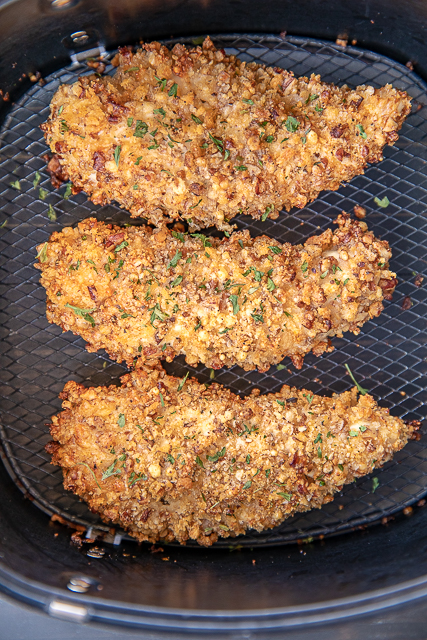 Air Fryer Pecan Chicken Tenders - our favorite thing to make in the air fryer! Chicken tenders coated in mayonnaise and honey mustard and rolled in panko bread crumbs, pecans and parmesan cheese. Seriously delicious! Can make in advance and refrigerate until ready to bake. Tastes great leftover too. #airfryer #chicken #chickentenders #easychickenrecipe chicken tenders in an air fryer basket