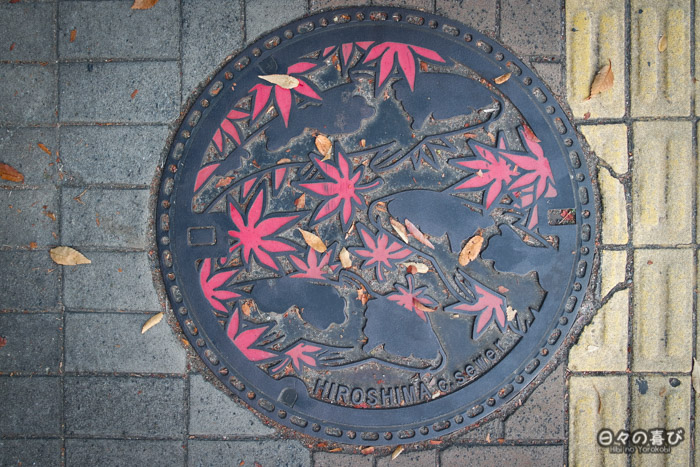 Les plaques d'égouts du quartier rappellent le surnom d'Hiroshima-jô, le "château de la carpe" Japanese manhole, plaque d'égout à motif de carpe et momiji, Hiroshima-shi