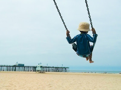 Boy swinging on a swing on a beautiful sandy beach with a pier and ocean in the background