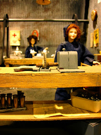 Dolls house miniature of a wartime munitions factory with two dolls at machines.