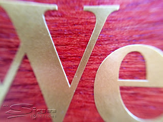 Close up of gold vinyl letter showing the thin edge of the vinyl applied to wooden board.