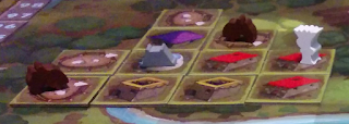 Eleven tiles on the board. The leftmost column has two livestock pen tiles in the bottom two spaces. The bottom tile has a cattle meeple on it. The next column has another pen at top, followed by a purple house tile, a blue house tile with a grey oven meeple on it, and a yellow house tile. The third column has the topmost space empty, with a pen containing a cattle meeple, then a red house tile, and a yellow house tile (the yellow house being adjacent to the yellow house in the previous column). The final column has two red house tiles in the bottom two spaces, so that the top one is adjacent to the red house tile in the previous column. There is also a white shrine meeple on the top tile in this column.