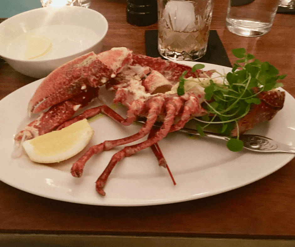 Half a lobster, cress garnish and a quarter of a lemon on a white plate.