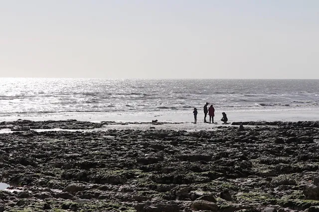 A rocky beach with a family silhouetted near the sea