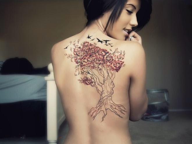 Linda mujer morena sonriendo , vemos que lleva un tatuaje de árbol de la vida en la espalda