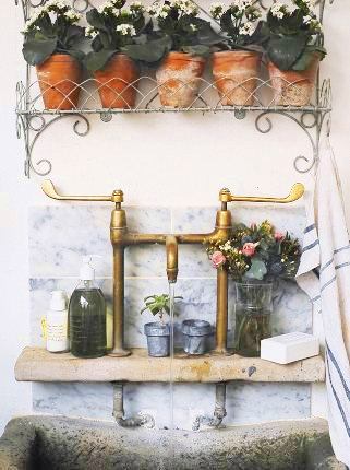 Farmhouse sink with Carrara marble backsplash and a small shelf to holding potted plants and a bouquet of flowers in a vase