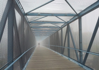 Cyclist emerging from the fog at the far end of a bike/pedestrian bridge.