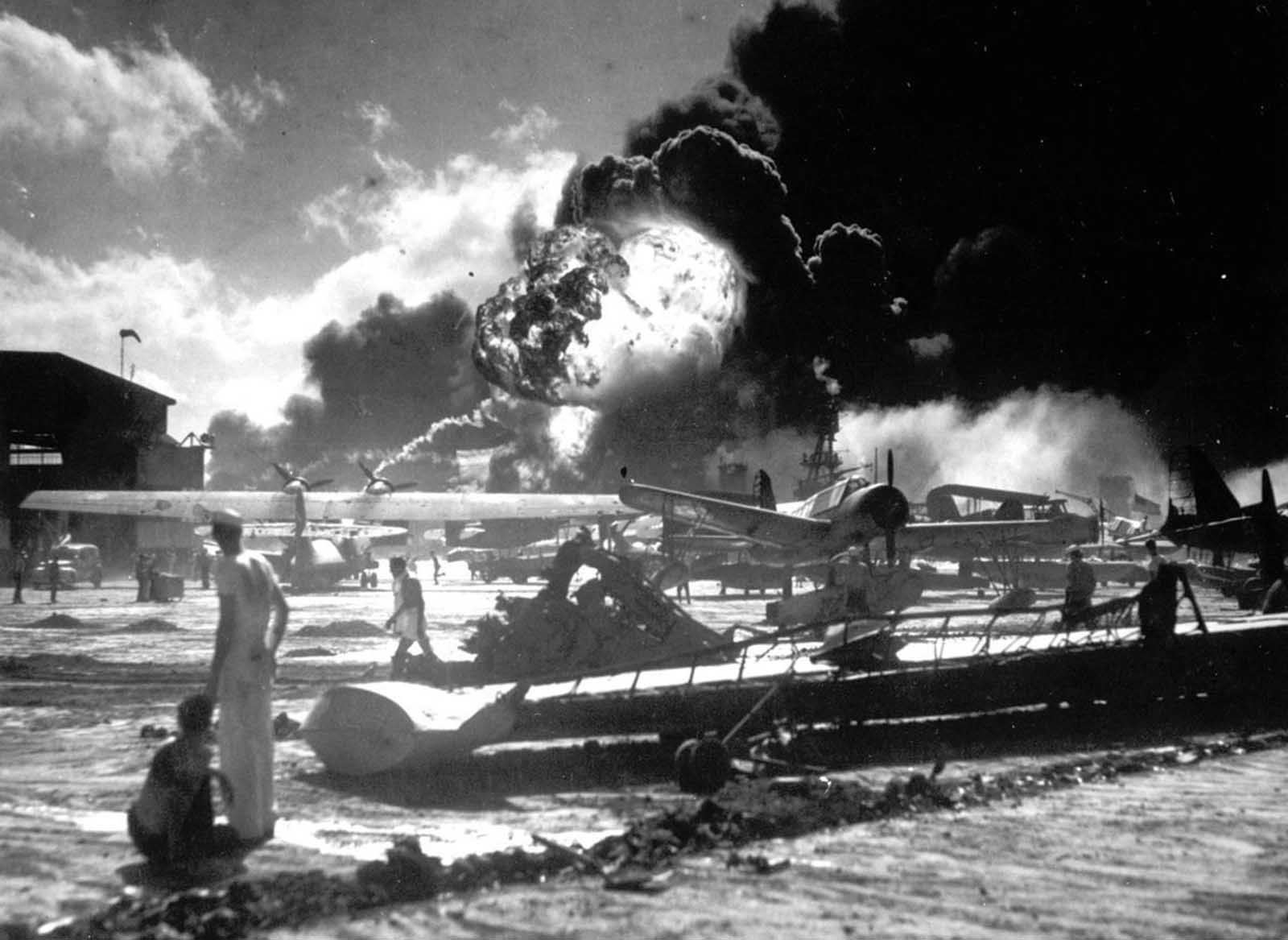 Sailors stand among wrecked airplanes at Ford Island Naval Air Station as they watch the explosion of the USS Shaw in the background, during the Japanese surprise attack on Pearl Harbor, Hawaii, December 7, 1941.