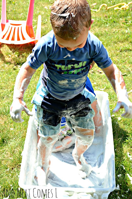Child standing in a sensory bin filled with rainbow soap foam bubbles