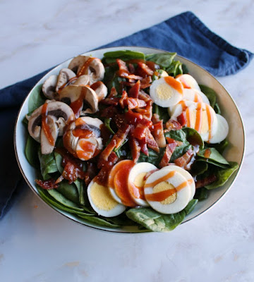 Close up bowl of spinach salad with red dressing drizzled over the top