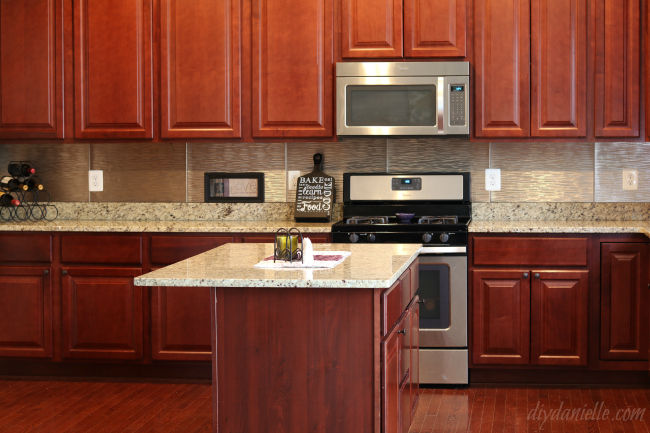 The Fasade Brushed Nickel backsplash matched with the cherry cabinets and granite counters. DIY Kitchen Backsplash in Brushed Nickel