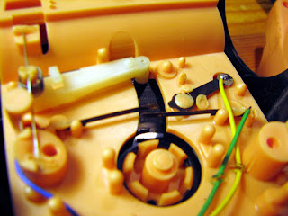 [Image: Still inside the speaker box, a slit reveals a little vinyl record underneath. A gramophone arm and needle are resting on it. Towards the end of the disc, there's a switch that seems to close an electronic circuit when the arm moves far enough.]