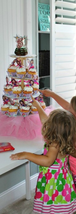 A little girl pointing to a cupcake tower.