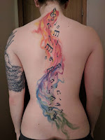 tatuaje notas musicales con acuarelas de colores en la espalda