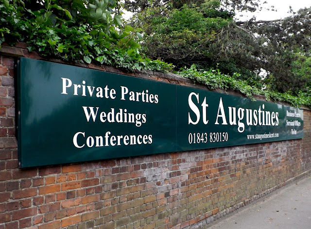 Long green metal sign, with white text with St Augustines and other details.