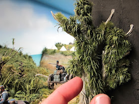 Fingers next to a cabbage tree in a diorama, showing scale..
