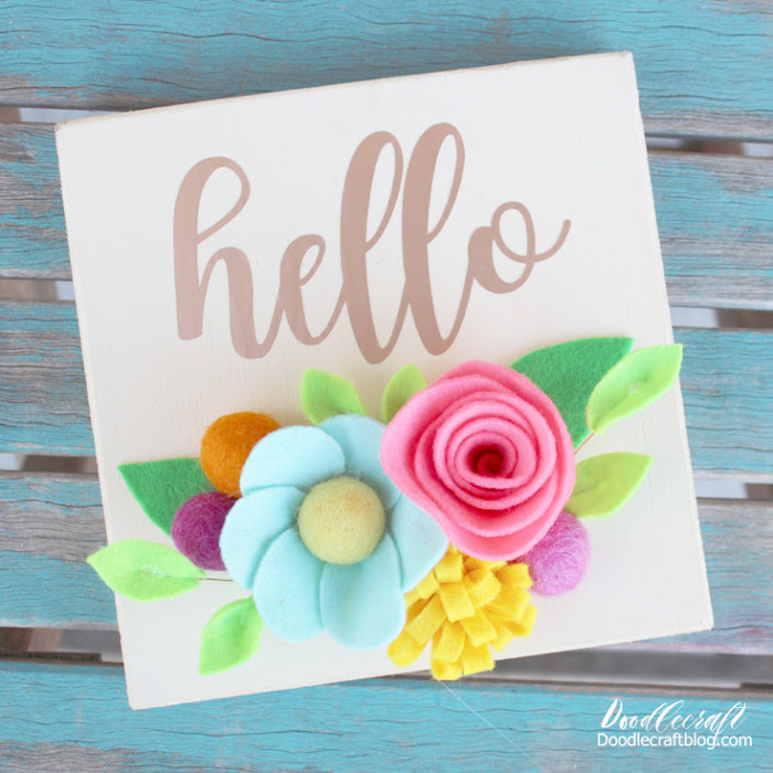 Hello Vinyl Wood Sign with Bright Felt Flowers! Isn't this hello sign perfectly bright and cheery with these colorful felt flowers!? Just a few supplies make this perfect Spring decoration for the mantle, bookshelf or in the entryway. Let me show you how to make felt flowers to add color to a vinyl wood sign for the perfect home decor piece!
