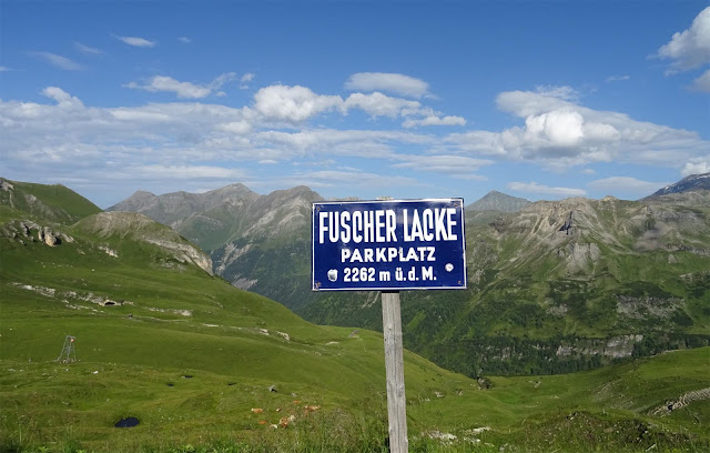 Blaues Blechschild am Fuscher Lake mit Bergkuppeln und grünen Hängen, Großglockner Hochalpenstrasse