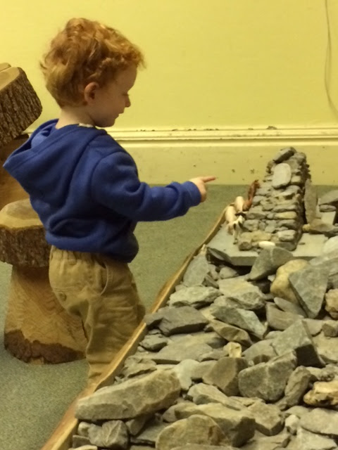 Toddler playing toy farm animals at a wooden table, covered in rocks