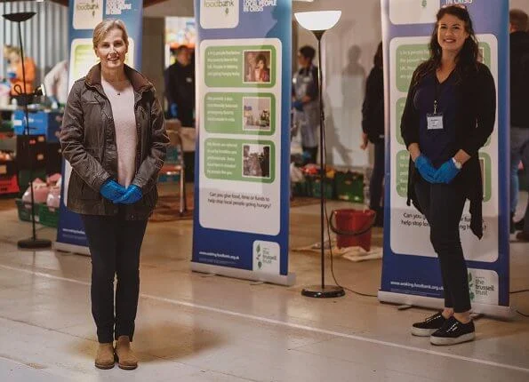 The Countess of Wessex visited the warehouse facility of the Woking Foodbank at Sheerwater. brown coat and pink sweater