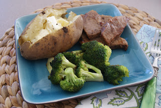 Sliced steak served with a baked potato and broccoli on a blue plate.