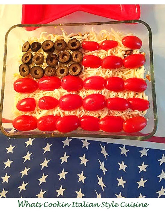 this is a dip with refried beans in a glass dish that has olives and tomatoes on top shaped in the a US flag