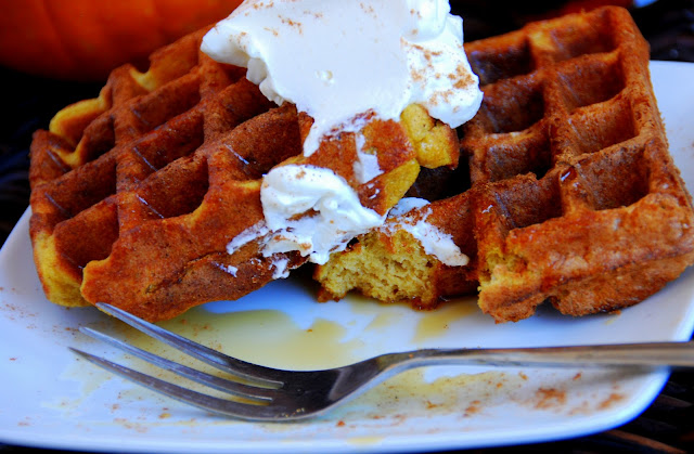 close up of pumpkin waffles with whipped cream on top with bite cut out of it