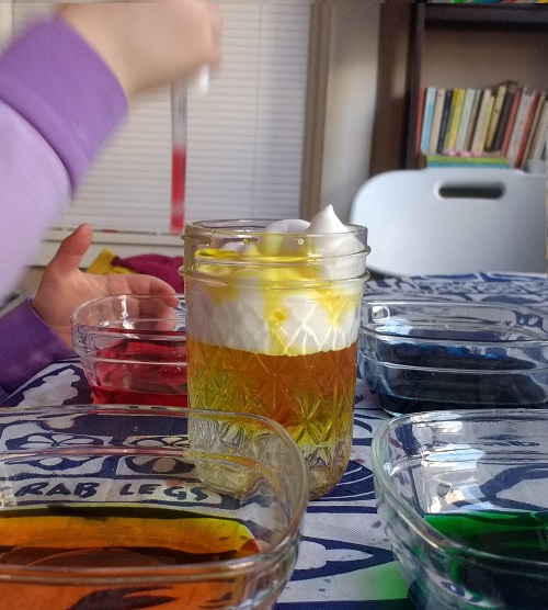 child dropping water of various colors into the shaving cream