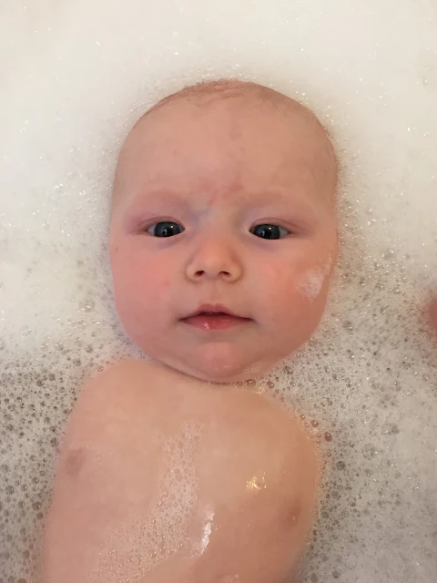 A baby's face floating in a bath surrounded by bubbles