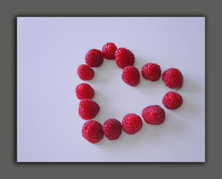 A card of red raspberries in the shape of a heart.