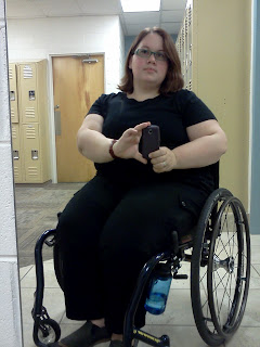 Author sitting in dark blue framed wheelchair with water bottle hanging off a wheel lock, wearing a black fitted tshirt and the black cargo pants mentioned in the paragraph