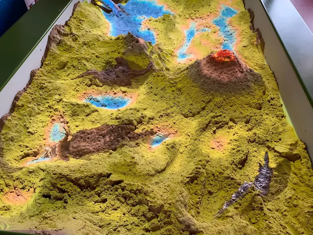 A sand pit that shows mountains and lakes and dinosaurs