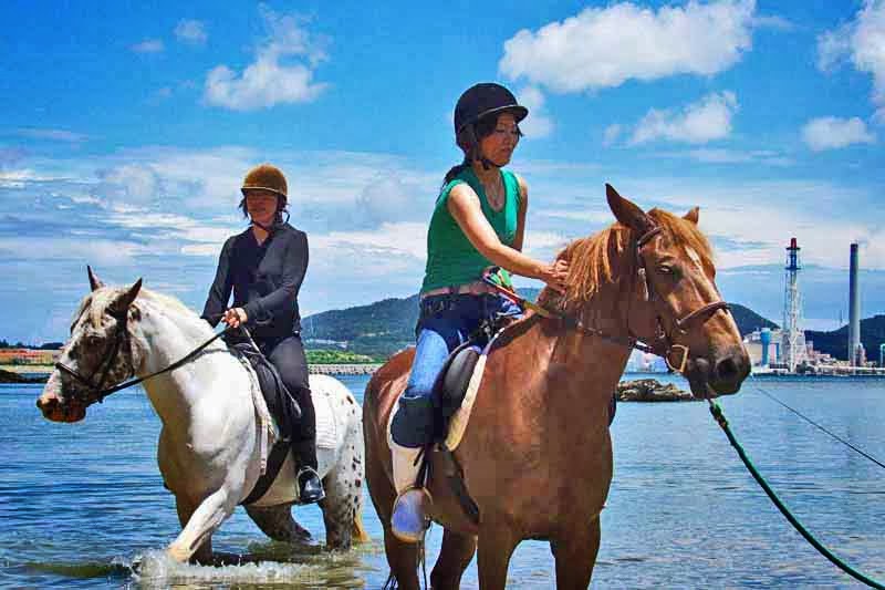 Two Japanese tourists ride horses at seashore