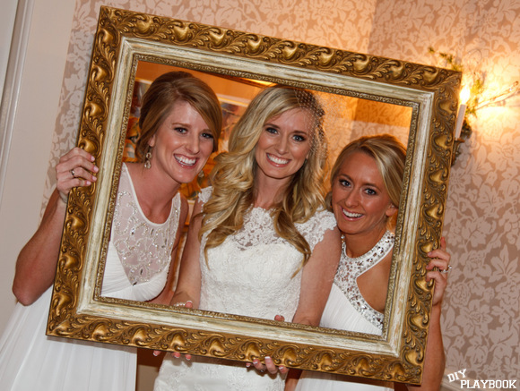 The bride and her bridesmaids pose with a frame in the photo booth area. 