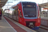 South Australian suburban electric passenger train; 4000 class  (no. 4003 entered service circa 2014) ) at a railway station platform. The train has silver sides with a red roof and red ends. Waiting passengers can be seen at the left of the picture.