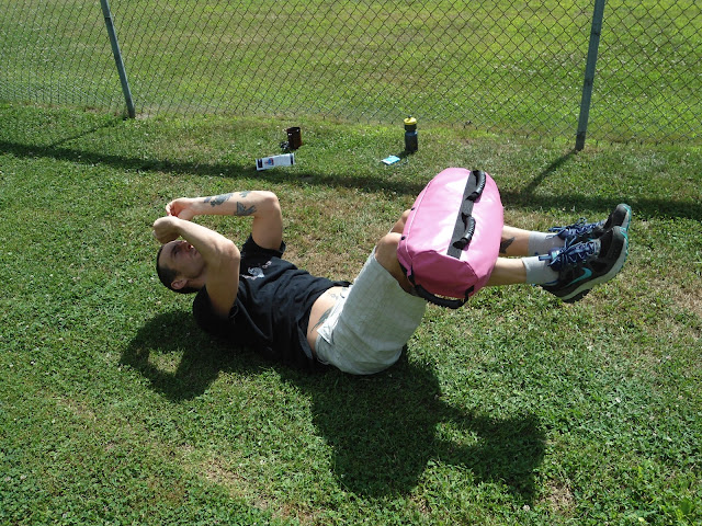 Man does abdominal crunches with The Ultimate Sandbag on his legs to provide added resistance while laying in a field