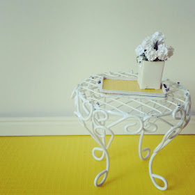 Modern one-twelfth scale white wire side table, holding a yellow and white tray with a white vase of daisies on it.