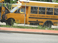 DCPS yellow school bus behind fence in parking lot with others