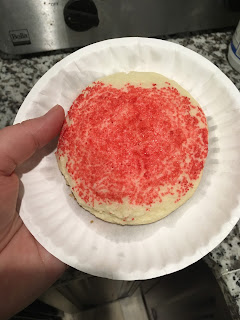 white paper dessert-sized plate filled with a single giant sugar cookie, dusted with red sugar sprinkles