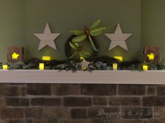 Mantle lighted with candles decorated with 5 different garland, wooden stars, and Luminaries in star shapes.
